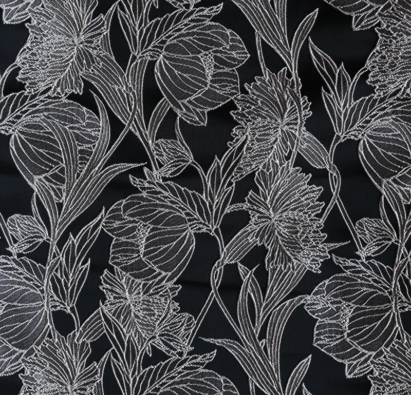 黒地に銀白色の線で大輪の花と葉を描いた織り生地のクローズアップ。蕾や花弁、茎葉が画面全体に連なり、輪郭線が浮かび上がる構図。