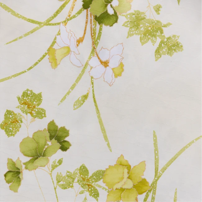 生成り地に黄緑の葉と白・淡黄の花を金線で描いた七五三着物の生地クローズアップ。植物文様が斜めに配され、金彩の点描があしらわれている。