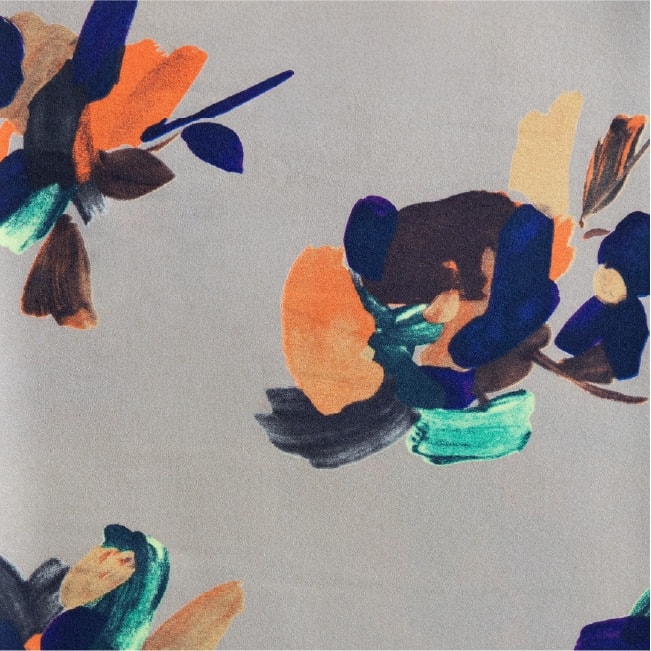 灰色地に抽象的な花柄を散らした生地 — オレンジ・濃紺・茶・エメラルドグリーンの絵筆風タッチで描かれた大柄模様の構図。