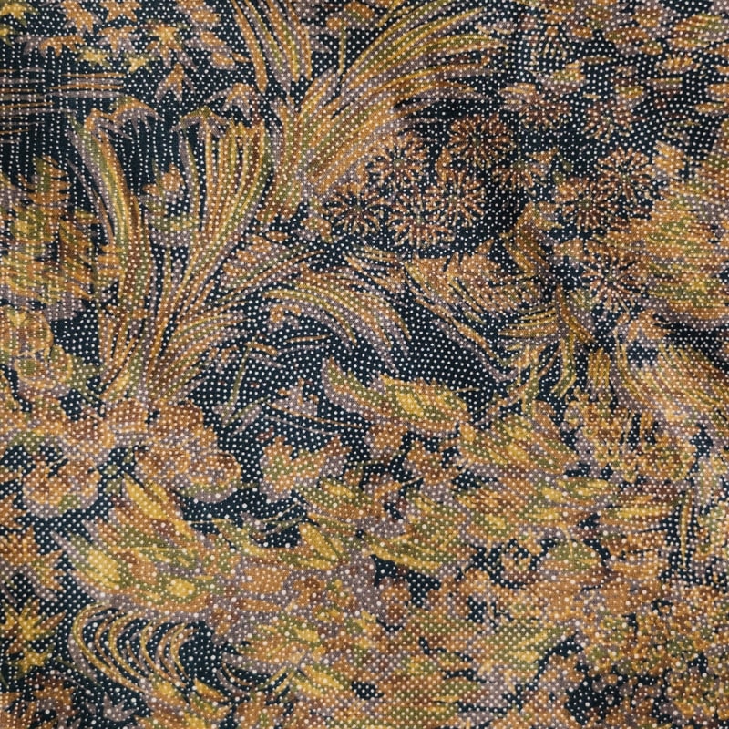 黒地に金茶・黄土・緑を用いた草花文様の織物クローズアップ — 細かな点描状の地紋と植物の枝葉や花を全面に配した構図。