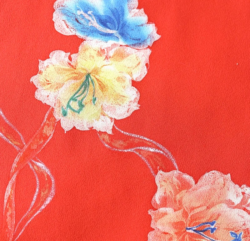 深紅の地に水彩調の花柄を配した七五三着物の生地クローズアップ — 青や黄、橙の花とつる模様が斜めに連なる構図。