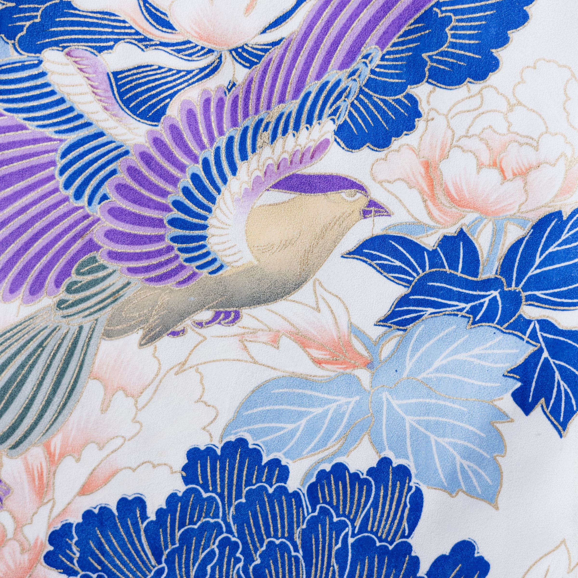 白地に青と紫の翼を広げた鳥を配した着物生地の接写 — 金彩で縁取られた牡丹や青系の葉、淡桃色の花が全体に染められている