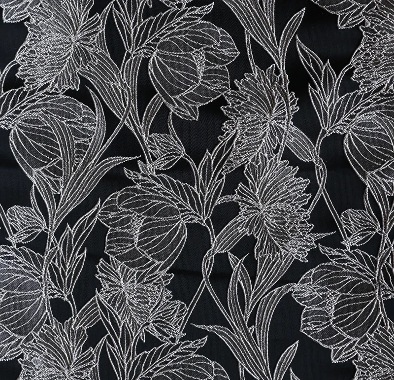 黒地に白い線描で花と葉を全面に表した着物生地のクローズアップ — 大ぶりの花や蕾、細い茎葉が連なり、黒の余白と白の輪郭が対比する構図。